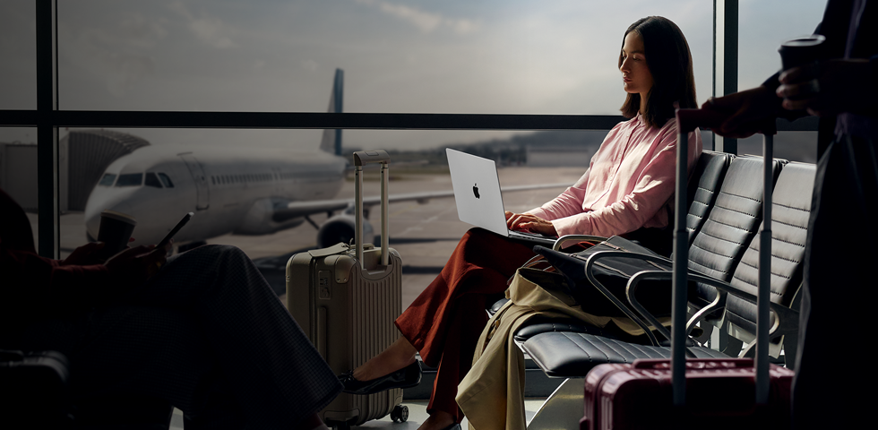 Un empleado escribe en un MacBook Pro de 14 pulgadas en plata desenchufado mientras espera su vuelo en la puerta de embarque