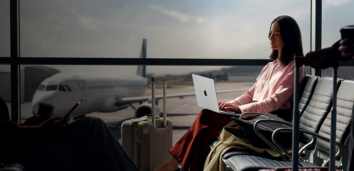 Un empleado escribe en un MacBook Pro de 14 pulgadas en plata desenchufado mientras espera su vuelo en la puerta de embarque