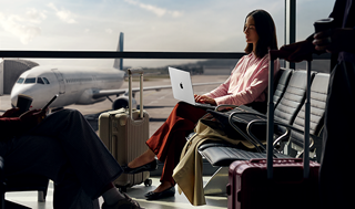 Un empleado escribe en un MacBook Pro de 14 pulgadas en plata desenchufado mientras espera su vuelo en la puerta de embarque