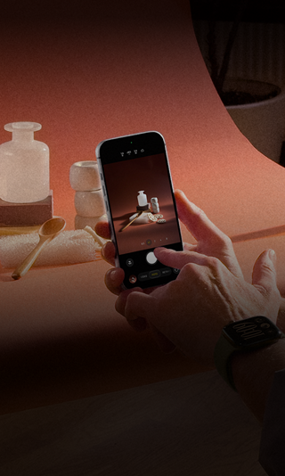 Sesión de fotos en un lugar de trabajo, una persona usa un iPhone para fotografiar productos sobre un fondo, otra sostiene una lámpara